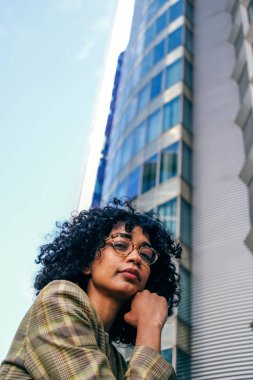 vertical portrait of elegant Latin American wearing eyeglasses lady under skyscraper