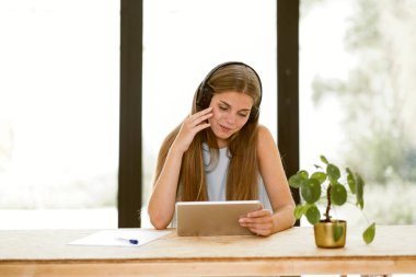 young woman student watching to tablet and listen to video podcasts or online lesson with wireless headphones