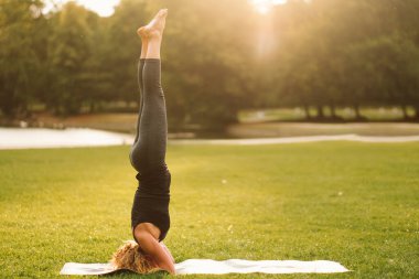 woman doing Sirsasana position or headstand on forearms yoga alone in the park in the sunrise warm light