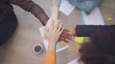 high-angle slow-motion shot of four hands, belonging to young men and women, coming together and then raising up in a gesture of celebration. The shot captures the moment of triumph, after completing a work project, a thesis, or an exam