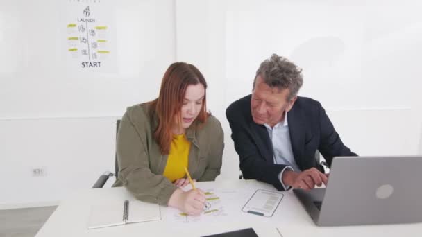 一个年轻的女人和一个年长的男人在一间现代化的办公室里一起工作 用笔记本电脑和平板电脑讨论摆在她们面前的一个项目 — 图库视频影像