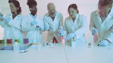 Odaklanmış bilim adamları modern bir laboratuvarda renkli sıvılarla kimyasal bir deney yürütüyorlar.