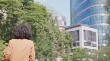 Modaya uygun Brezilyalı kadın şehir merkezinin gökdelenlerinin altında parkta yürüyor dinleniyor ve telefonla mesaj yazıyor.