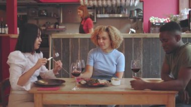 Çeşitli arkadaş grupları restoranda birlikte yemek yiyorlar. Çeşitli insanlar sohbet ediyor ve yemek ve şarabın tadını çıkarıyorlar. Garsonlar arka planda yavaş çekim videolarını izliyorlar.