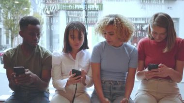 Bir pencerenin kenarında oturan bir grup genç yetişkin akıllı telefonlarla meşgul. Modern dijital etkileşim ve sosyal davranışlar sıradan bir ortamda. Yavaş çekim videosu