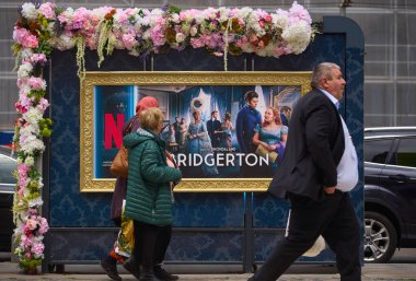 Bükreş, Romanya. 15 Mayıs 2024: Bükreş 'in merkezindeki çiçek desenli otobüs durağında Netflix Bridgerton TV serisinin reklamının önünden geçen insanlar görülüyor