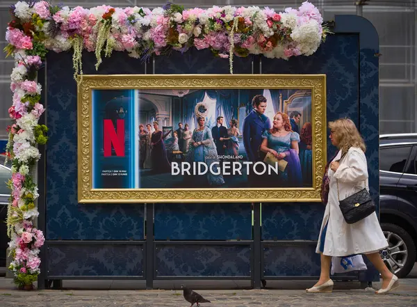 Bükreş, Romanya. 15 Mayıs 2024: Bükreş 'in merkezindeki çiçek desenli otobüs durağında Netflix Bridgerton TV serisinin reklamının önünden geçen insanlar görülüyor