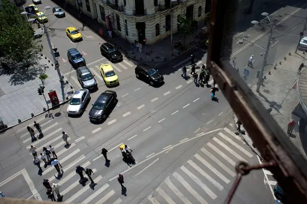 Bükreş, Romanya. 7 Mayıs 2025: Yabancı kökenli Glovo gıda kuryeleri, Romanya 'nın başkenti Bükreş' te üst pencerelerden görülen yoğun bir kavşaktan geçerken yiyecek dağıtıyorlar.