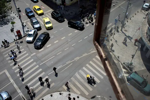 Bükreş, Romanya. 7 Mayıs 2025: Yabancı kökenli Glovo gıda kuryeleri, Romanya 'nın başkenti Bükreş' te üst pencerelerden görülen yoğun bir kavşaktan geçerken yiyecek dağıtıyorlar.