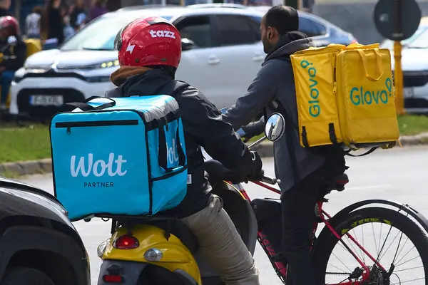 Bükreş, Romanya. 13 Mayıs 2025: Glovo ve Wolt gıda dağıtım kuryeleri, yabancı kökenli işçiler, Romanya 'nın Bükreş kentinde gıda dağıtımı yapıyorlar.