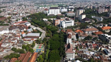 Malang, Indonesia  September 20th, 2024 A drone-captured image of an urban area, with buildings nestled among lush green trees. The cityscape showcases a balance of development and greenery, adding to the charm of the area. clipart