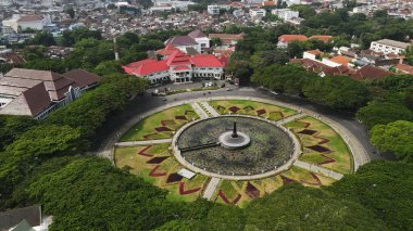 Malang, Indonesia  September 20th, 2024 A drone-captured image of an urban area, with buildings nestled among lush green trees. The cityscape showcases a balance of development and greenery, adding to the charm of the area. clipart