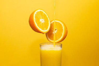 pouring juice into a glass from half an orange on an orange background
