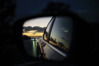 Bir arabanın yan aynasında akşam otobanının yansıması.