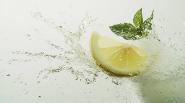 Yeşil yapraklı sarı limon dilimi. Grafik tasarımı ya da duvar kâğıdı için el değmemiş beyaz bir arka plana nazikçe su sıçratıyor. Meyveler narenciye ve yüksek C vitamini içerir..  