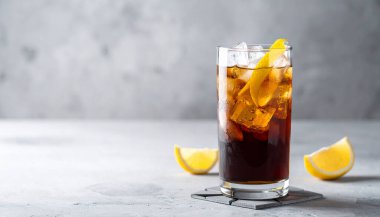 Viski bardağında, buz küplerinde, limon bükümünde, geometrik bardak altlığında tonik içeren siyah soğuk bira..  