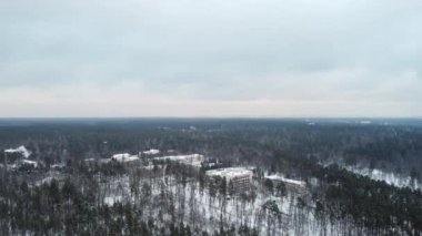 Buildings and houses in the middle of the forest in winter with snow. Shooting from a height on a quadcopter.