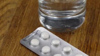 Bir bardak suyla birlikte su toplamış beyaz hapların yakın çekim rotasyonu..