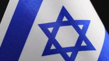 Koyu bir arkaplan üzerinde dönen İsrail bayrağına yakın plan.