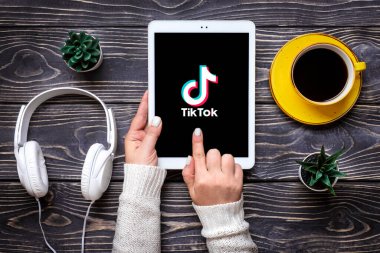 Bangkok, Tayland Eylül 2022 Smartphone Tik Tok uygulama simgesi, ekranda logo, beyaz kulaklıklar, ahşap masa üzerinde bir fincan kahve Moda Sosyal medya ağı konsepti.