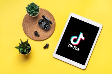 Bangkok, Tayland Ekim 2022 Tablet Tik Tok uygulama simgesi, ekranda logo, kablosuz kulaklık, sarı masadaki şarj kapsülü Moda Sosyal medya ağı konsepti Düz.