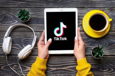 Bangkok, Tayland Ekim 2022 Tablet Tik Tok uygulama simgesi, ekranda logo, kablosuz kulaklık, ahşap masa üzerindeki şarj kapsülü Moda Sosyal medya ağı konsepti.