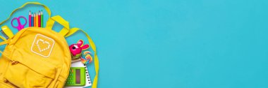 Okula dönüş, eğitim konsepti okul malzemeleriyle dolu sarı sırt çantası - not defteri, kalemler, silgi gökkuşağı, mavi arkaplanda izole edilmiş numaralar Üst görünümde kopya alanı kompozisyon banner.