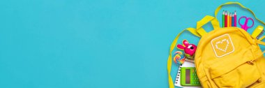 Okula dönüş, eğitim konsepti okul malzemeleriyle dolu sarı sırt çantası - not defteri, kalemler, silgi gökkuşağı, mavi arkaplanda izole edilmiş numaralar Üst görünümde kopya alanı kompozisyon banner.