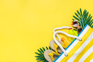 Yüzme aksesuarları - çizgili plaj çantası, güneş kremi, kalp şeklinde gözlük, sarı kaplama terliği, sarı arka planda deniz kabuğu..