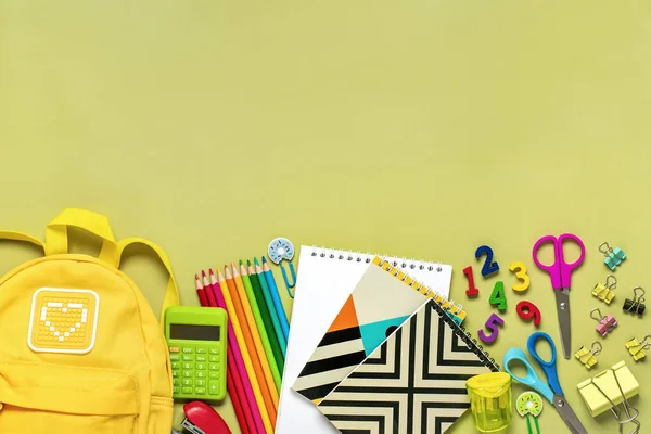 Back to school, education concept Yellow backpack with school supplies - notebook, pens, eraser rainbow, numbers isolated on green background Top view Copy space Flat lay composition Banner.
