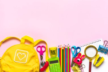 Back to school, education concept Yellow backpack with school supplies - notebook, pens, eraser rainbow isolated on pink background Top view Copy space Flat lay composition Banner.
