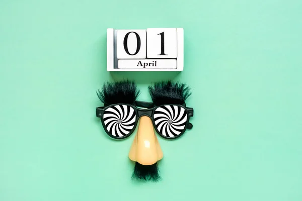 funny face - fake eyeglasses, nose and mustache, calendar date 01 April on green background Happy fools day concept 1st April party Holiday greetind card.