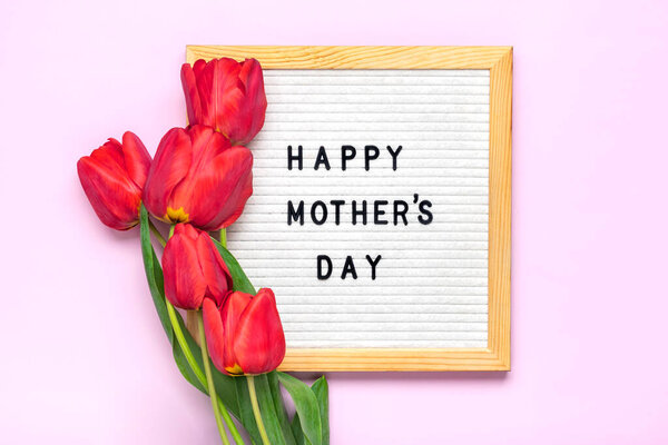 Доска из войлока с текстом С Днем Матери, букет из красных тюльпанов на розовом фоне Открытка на заднем плане.