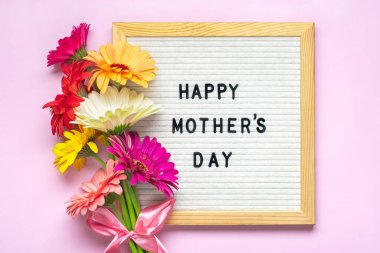 Felt board with text Happy Mothers day, colorful gerberas bouquet on pink backround greeting holiday card Flat lay Top view.