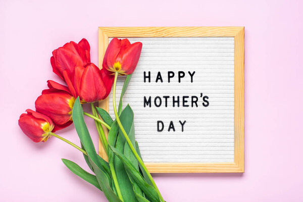 Доска из войлока с текстом С Днем Матери, букет из красных тюльпанов на розовом фоне Открытка на заднем плане.