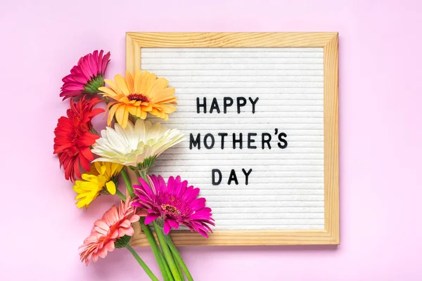 Felt board with text Happy Mothers day, colorful gerberas bouquet on pink backround greeting holiday card Flat lay Top view.