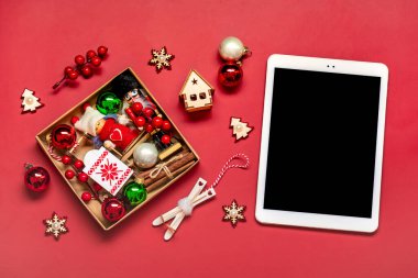 Siyah ekranlı en üstteki tablet, kırmızı masadaki Noel kutusu ve dekor Tatil alışveriş listesi, Mutlu Yıllar, çevrimiçi dükkan, hediyeler seçer, Mockup satın alır.