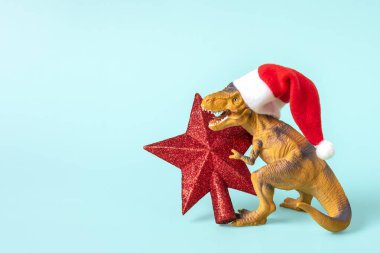 Kırmızı Noel Baba şapkalı dinozor Rex 'in mavi arka planda bir yıldızı var. Yeni yıl arifesinde ya da Noel arifesinde. Mutlu Noel' ler için yaratıcı bir fikir..