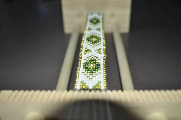 stock image A close-up of hands crafting a beaded bracelet on a specialized loom. The bracelet features a traditional pattern with colorful beads. Tools and materials are neatly arranged, showcasing precise, skil