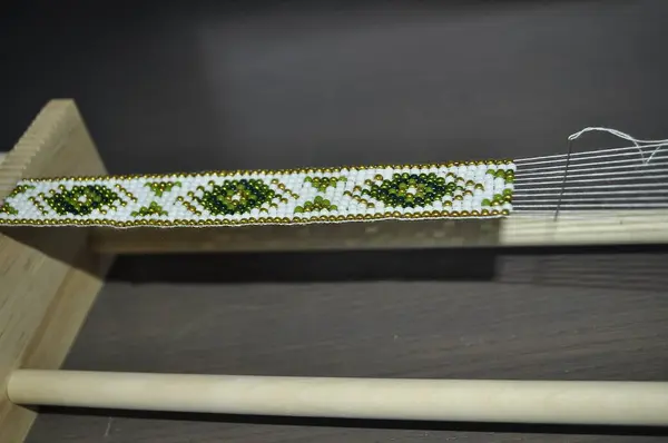 stock image A close-up of hands crafting a beaded bracelet on a specialized loom. The bracelet features a traditional pattern with colorful beads. Tools and materials are neatly arranged, showcasing precise, skil