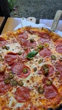 Bir kafede sosisli ve zeytinli büyük pizza.