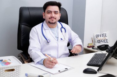 Klinikte elinde kalemle oturan genç bir doktor var.. 