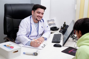 Genç bir doktor klinikte oturmuş hastasıyla konuşuyor ve gülümsüyor..