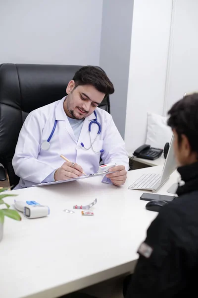 若い医者が診療所に座って紙に薬を書いてる — ストック写真