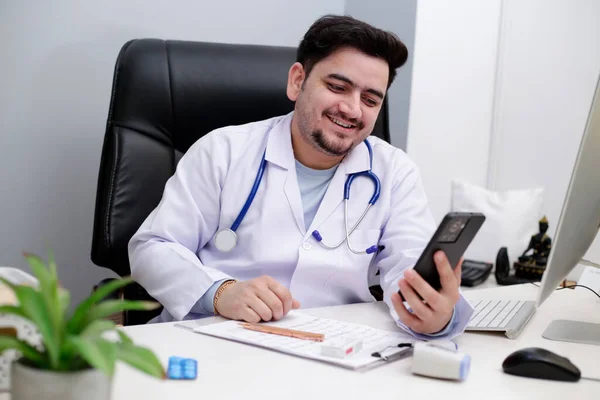 Młody Lekarz Siedzi Klinice Ogląda Coś Komórce Uśmiecha Się — Zdjęcie stockowe