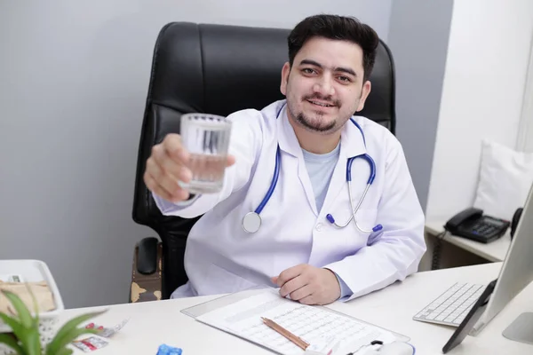 Médico Joven Está Sentado Silla Clínica Sosteniendo Vaso Agua Mano —  Fotos de Stock