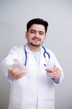 Bir elinde su bardağı, diğer elinde su şişesi olan genç bir doktor ayakta duruyor..