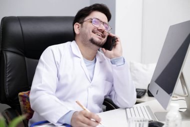 Genç bir doktor klinikte oturuyor ve telefonla konuşuyor..