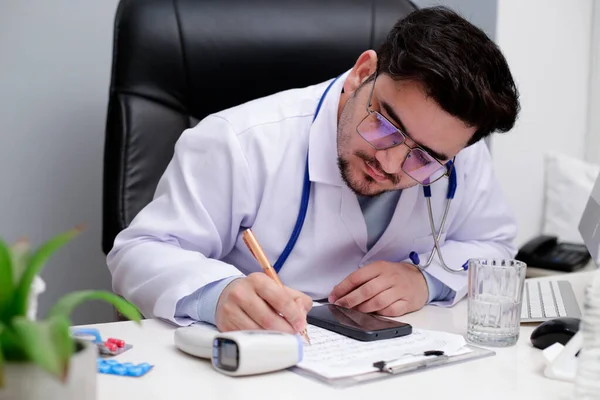 Médico Joven Está Sentado Clínica Escribiendo Algo Papel Con Bolígrafo —  Fotos de Stock