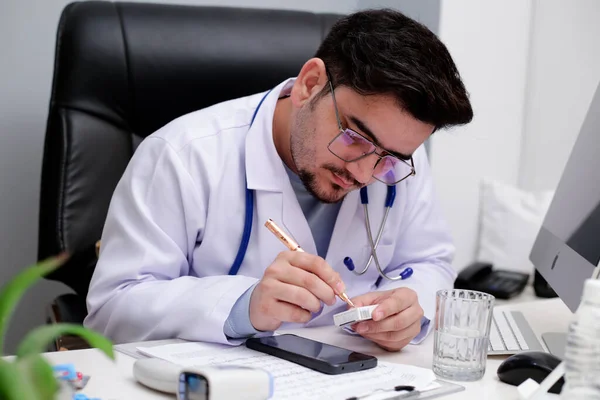 Jovem Médico Está Sentado Clínica Segurando Caneta Mão Escrevendo Algo — Fotografia de Stock